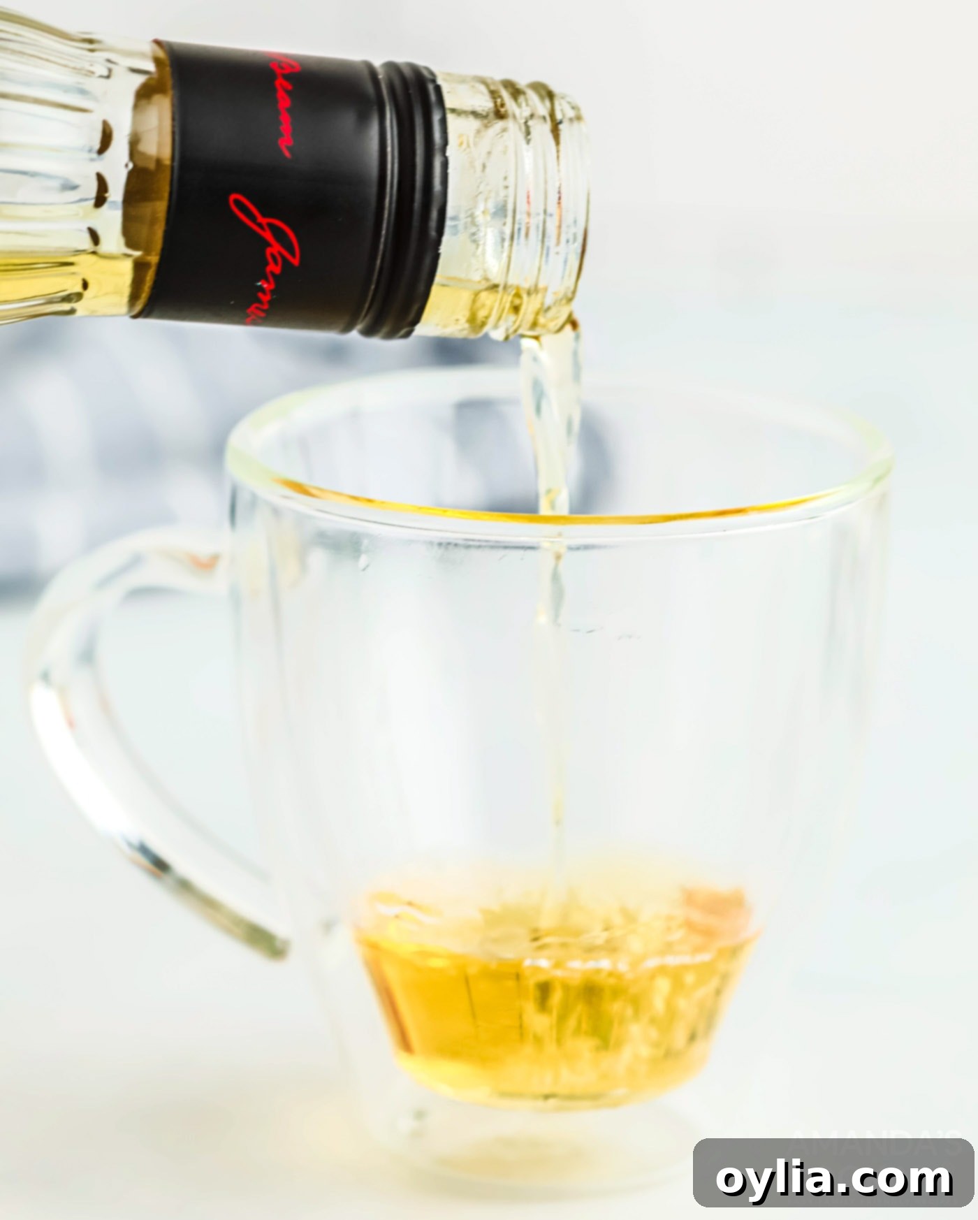 Pouring apple whiskey into a mug, the first step in making the cocktail