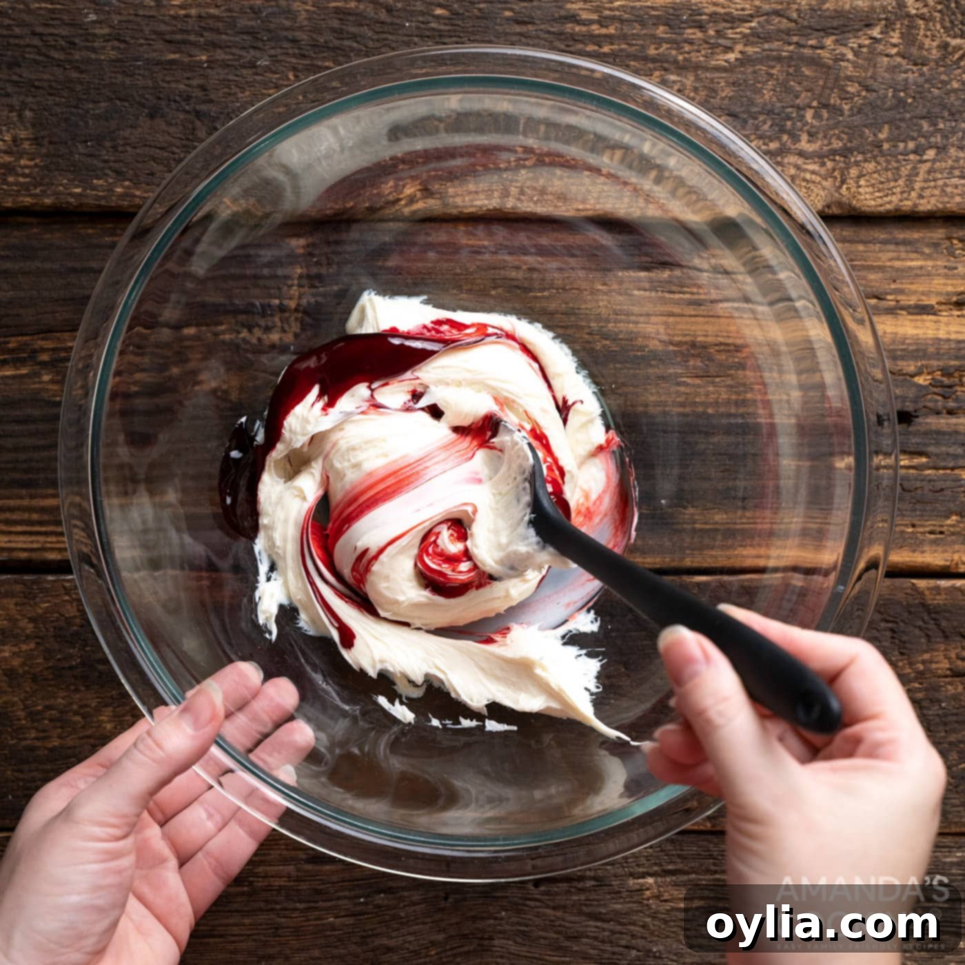 Mixing red gel food coloring into vanilla frosting in a bowl