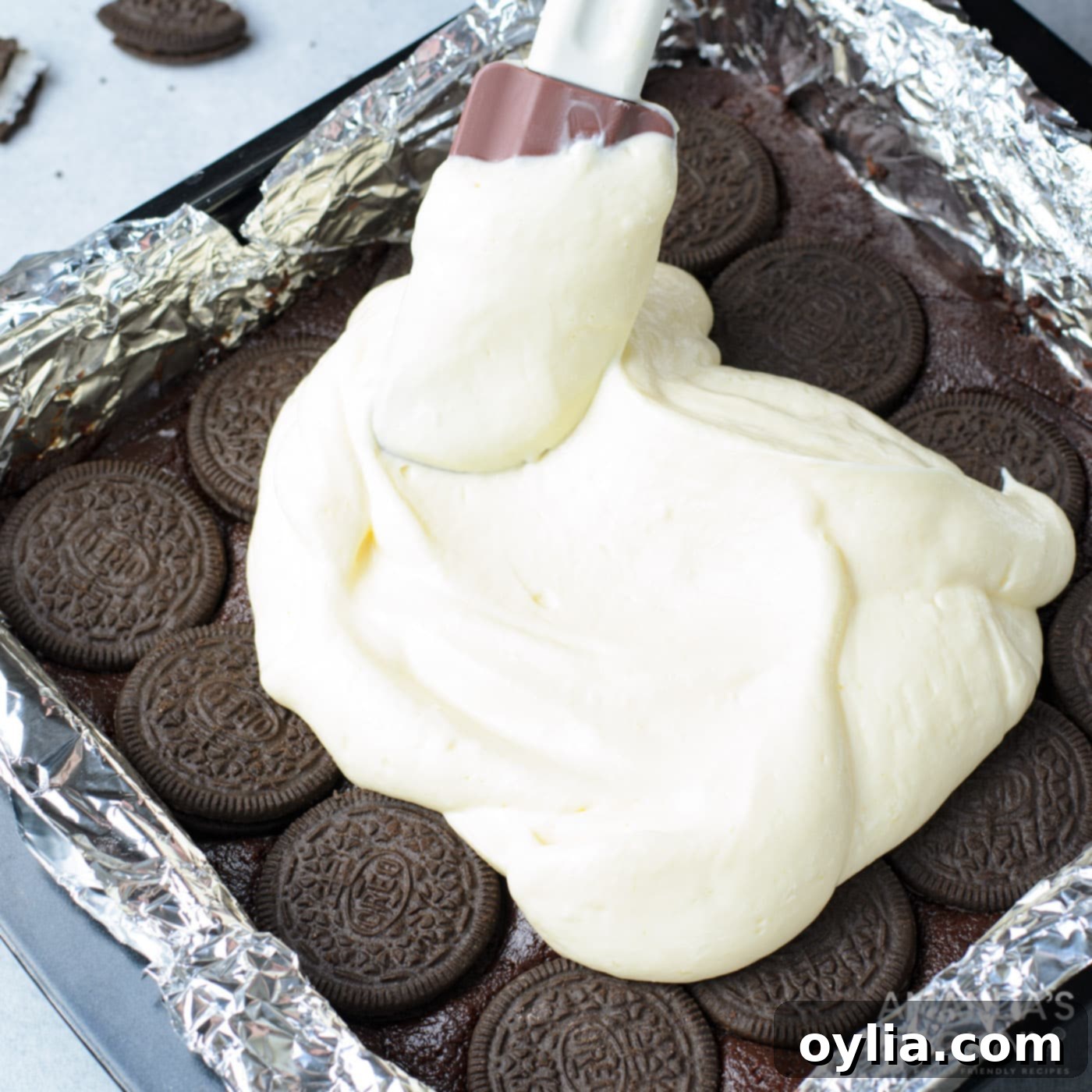 spatula smoothing out cheesecake layer on top of oreo brownies