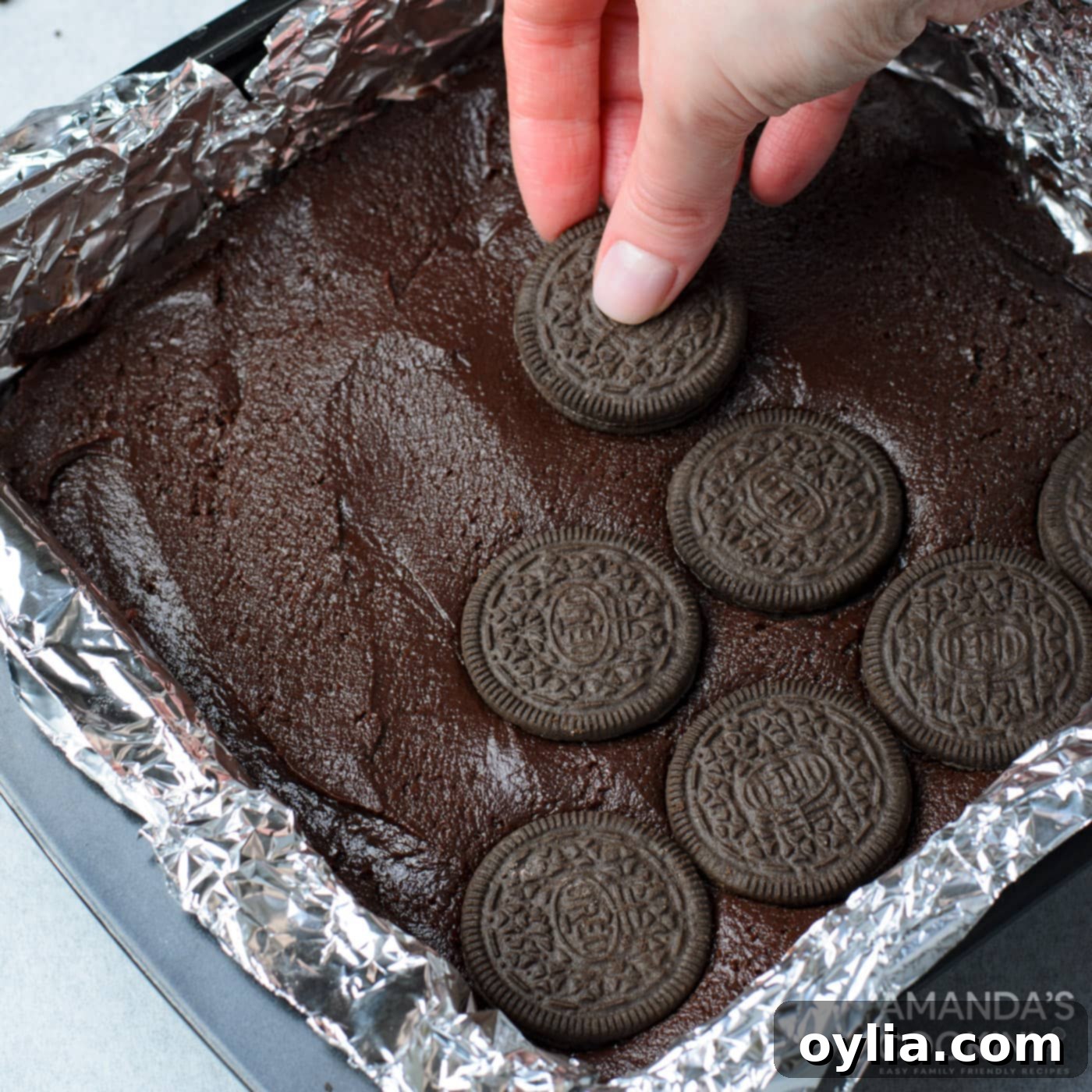 hand placing oreo cookies on top of brownie batter in a pan