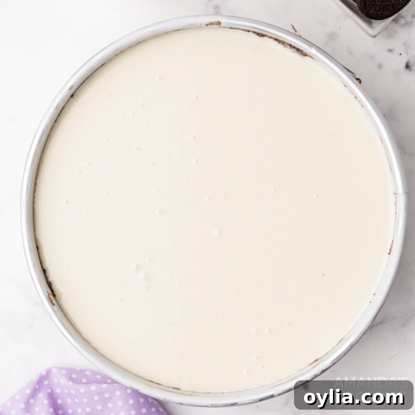 White chocolate ganache being poured over the top of the Oreo cheesecake.