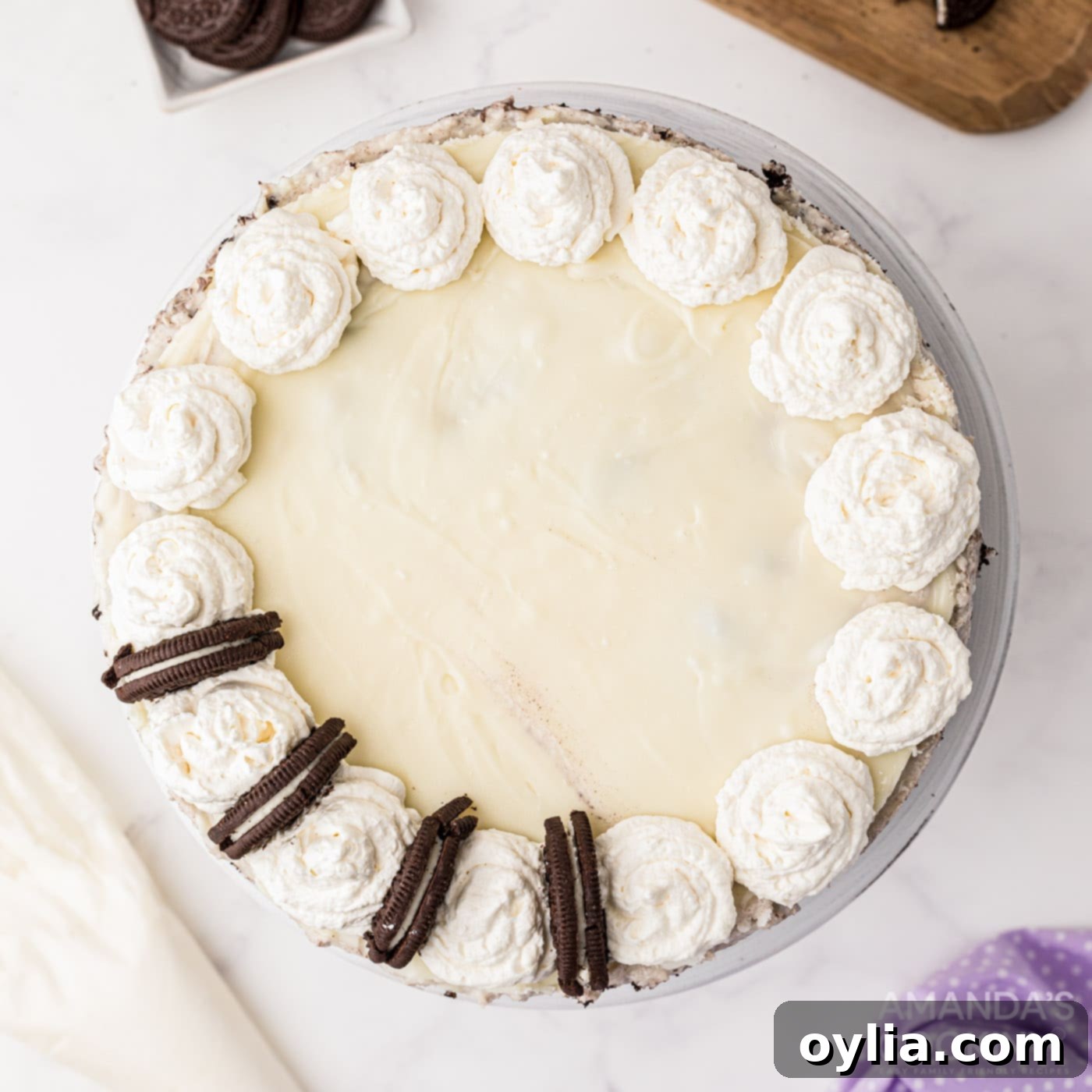 Finished Oreo cheesecake with whipped cream swirls and Oreo halves on top, ready to serve.