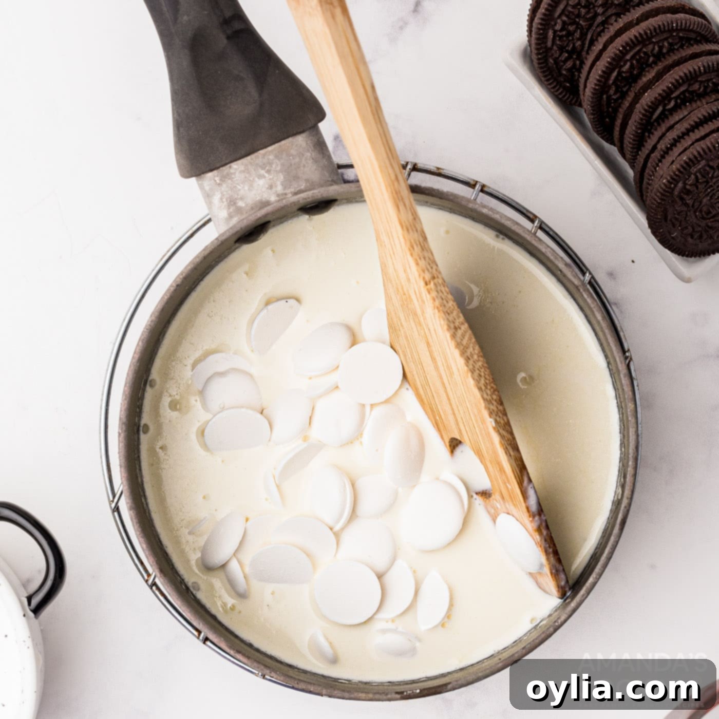 White chocolate wafers melting into warm heavy cream in a saucepan, creating ganache.