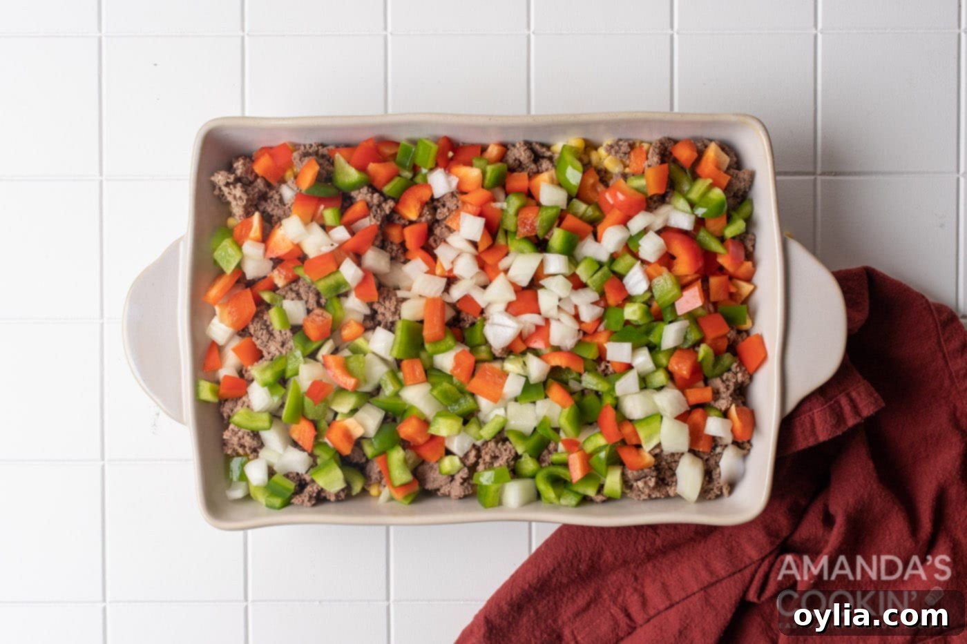 Stacked Supper Supreme 8 chopped peppers and onion on top of ground beef in a baking dish