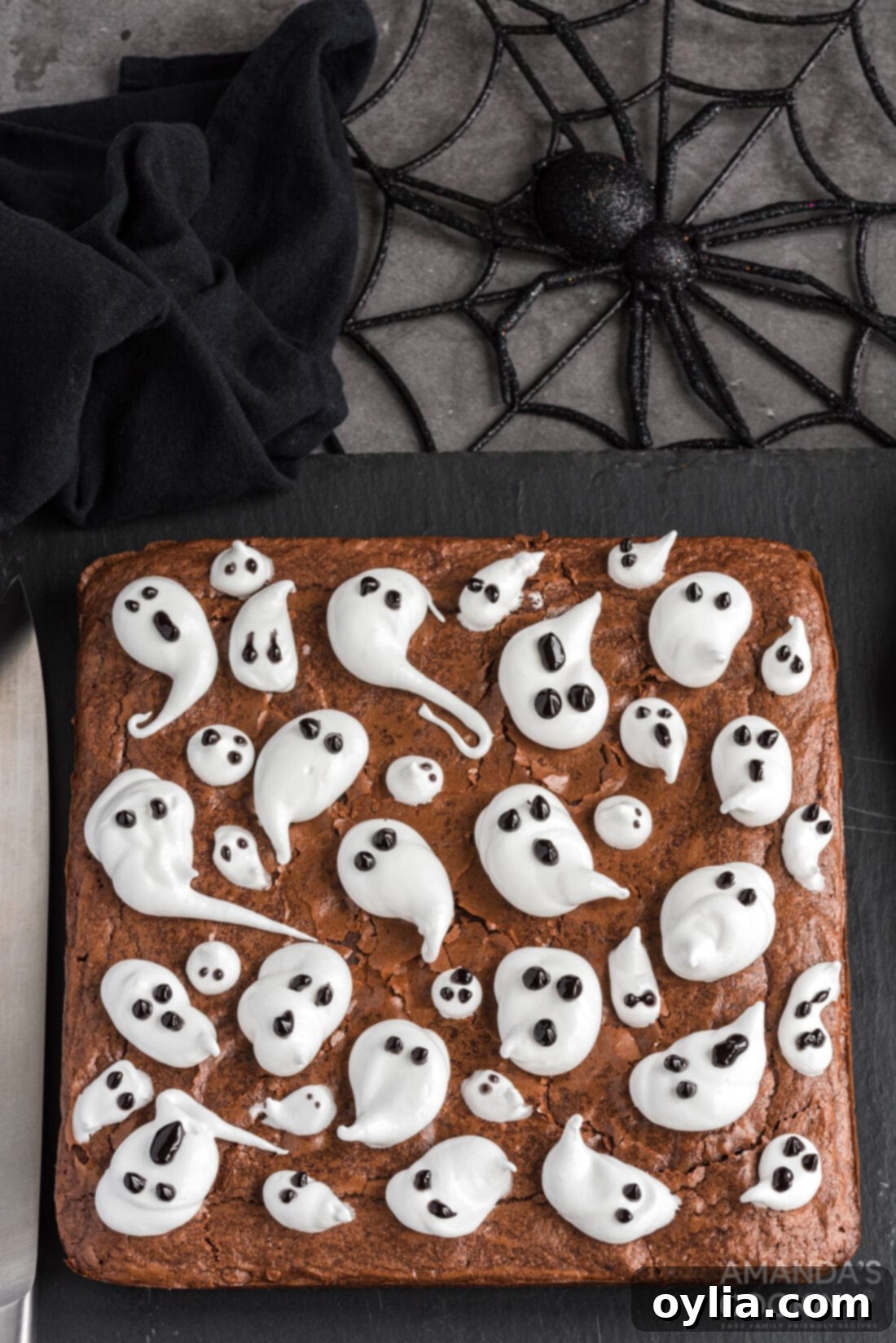 overhead view of Ghost Brownies, featuring multiple brownies topped with white marshmallow ghosts and black gel icing eyes and mouths, arranged on a cooling rack.