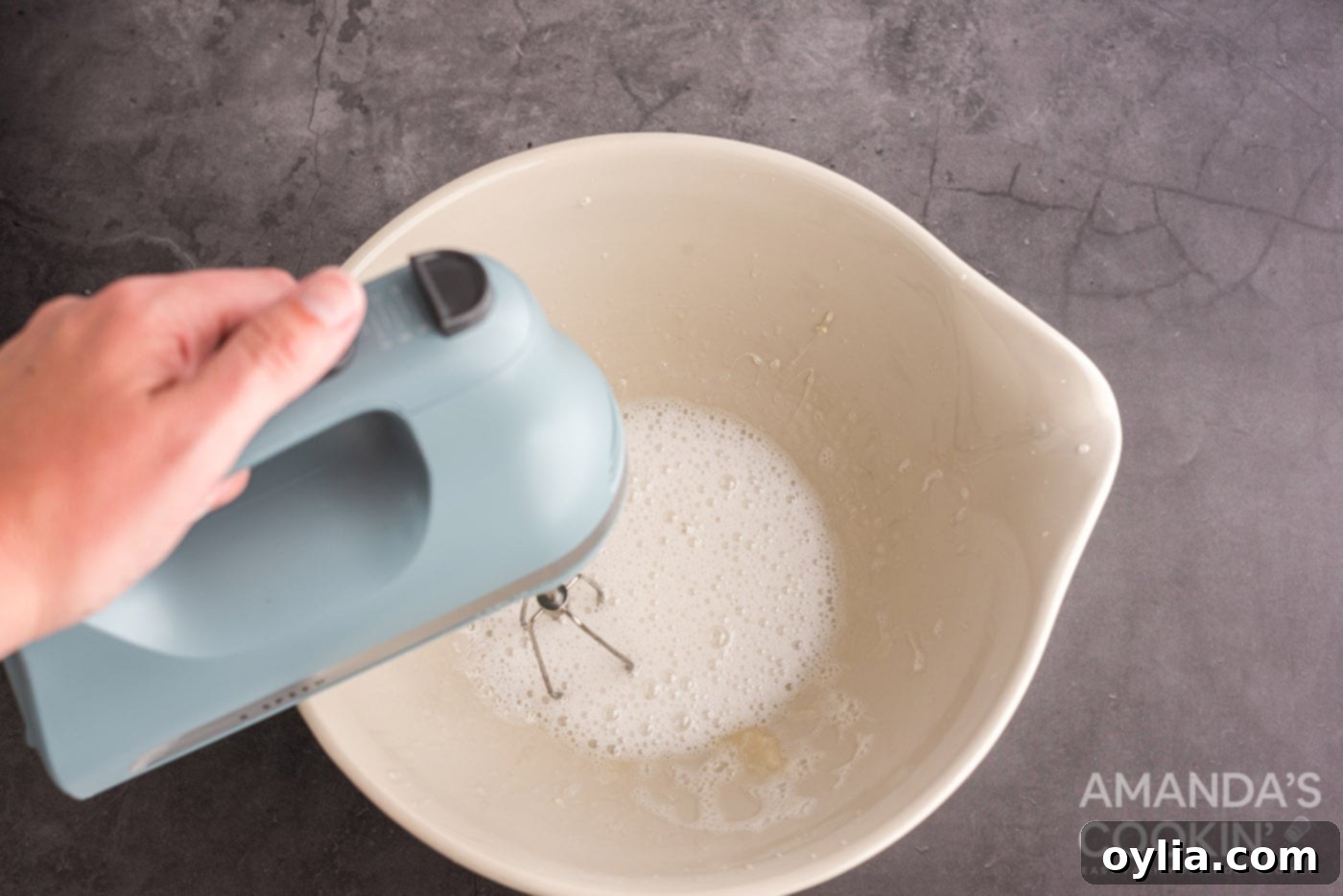 mixing gelatin and sugar water in a bow with hand mixer, creating fluffy marshmallow.