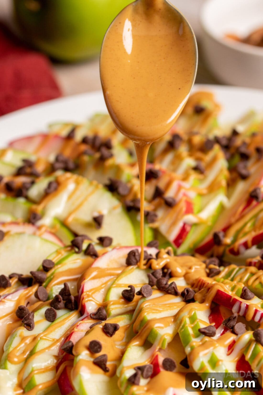 Hand drizzling creamy peanut butter over crisp apple slices for an apple nacho base