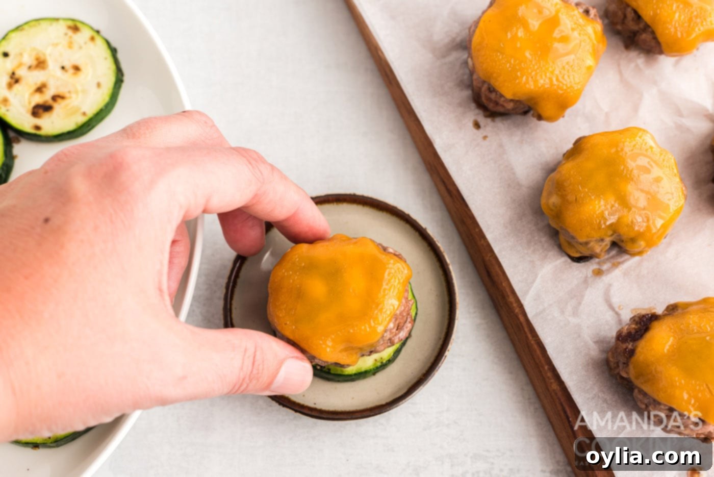 hand placing cheeseburger on zucchini round