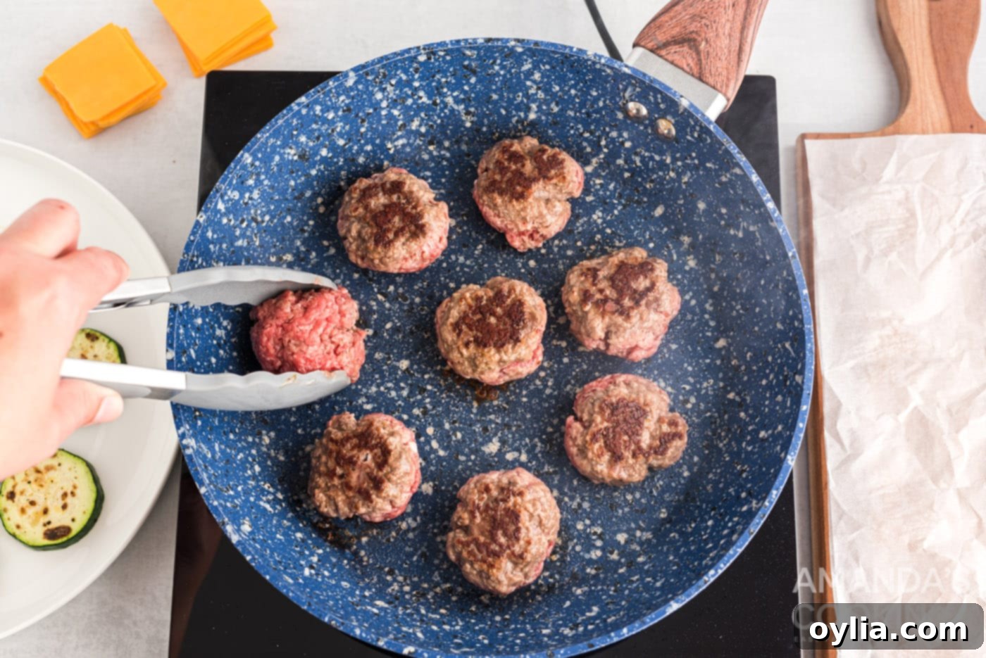 tongs flipping burger patty in a skillet