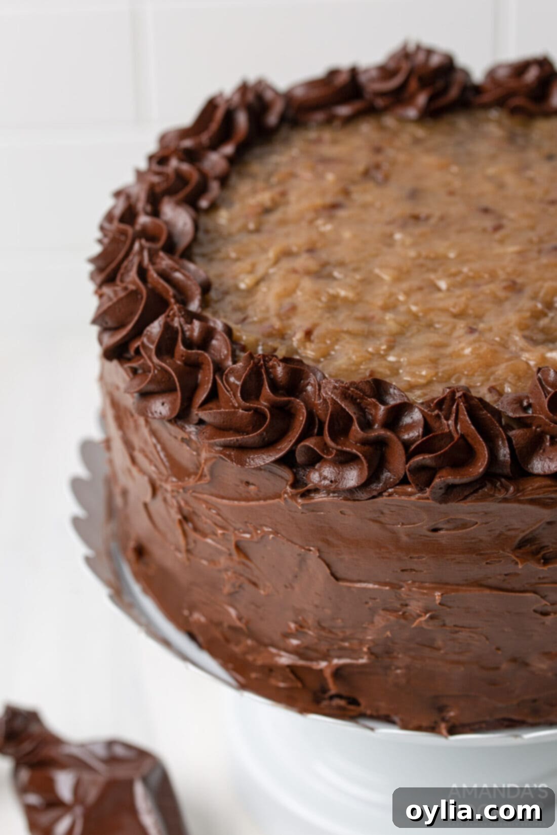 A stunning, multi-layered German Chocolate Cake on a white cake stand, showcasing its moist chocolate layers, rich coconut-pecan filling, and smooth chocolate frosting.