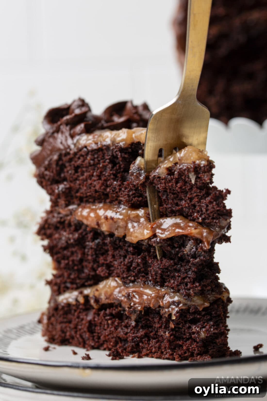 A fork taking a bite from a perfectly sliced piece of German Chocolate Cake, revealing the moist chocolate layers and the rich coconut-pecan filling.