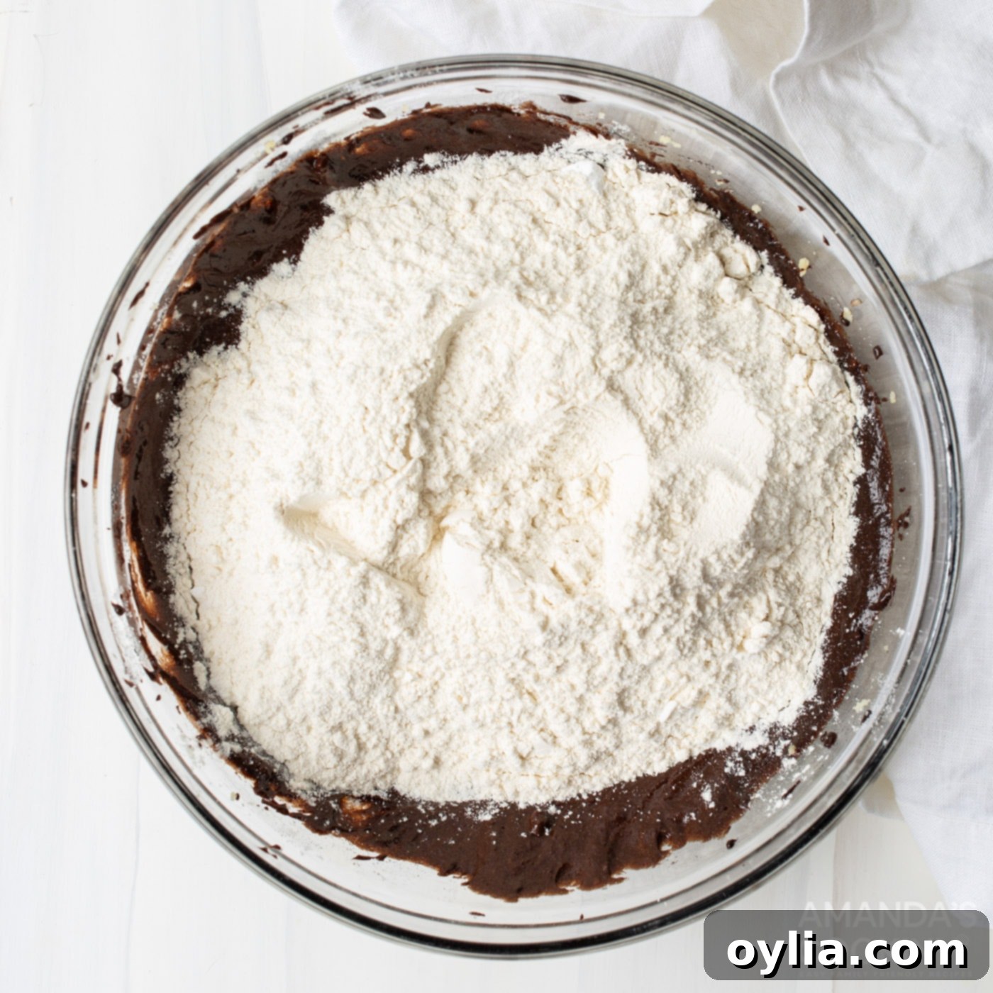 Adding flour in batches to the chocolate cake batter in a mixing bowl.