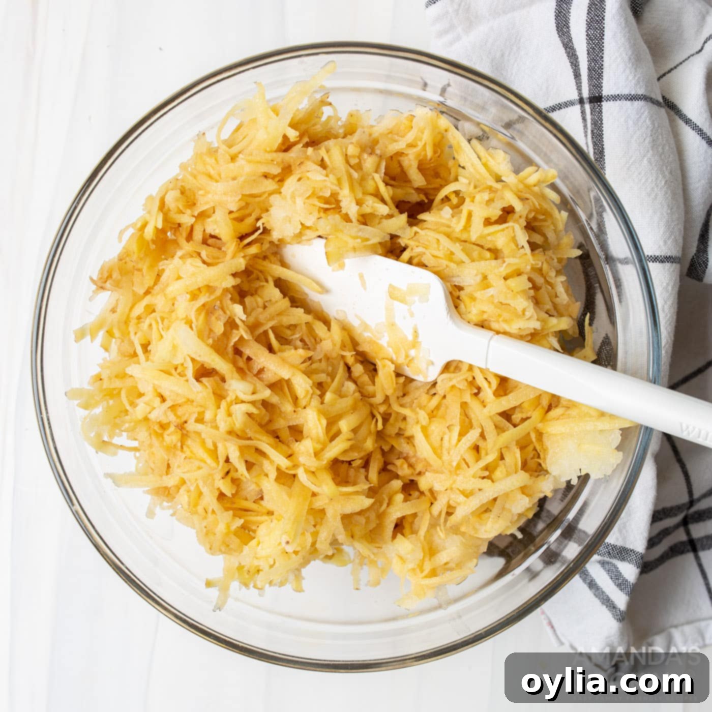 Coarsely grated potatoes and onion in a colander, illustrating the draining process.
