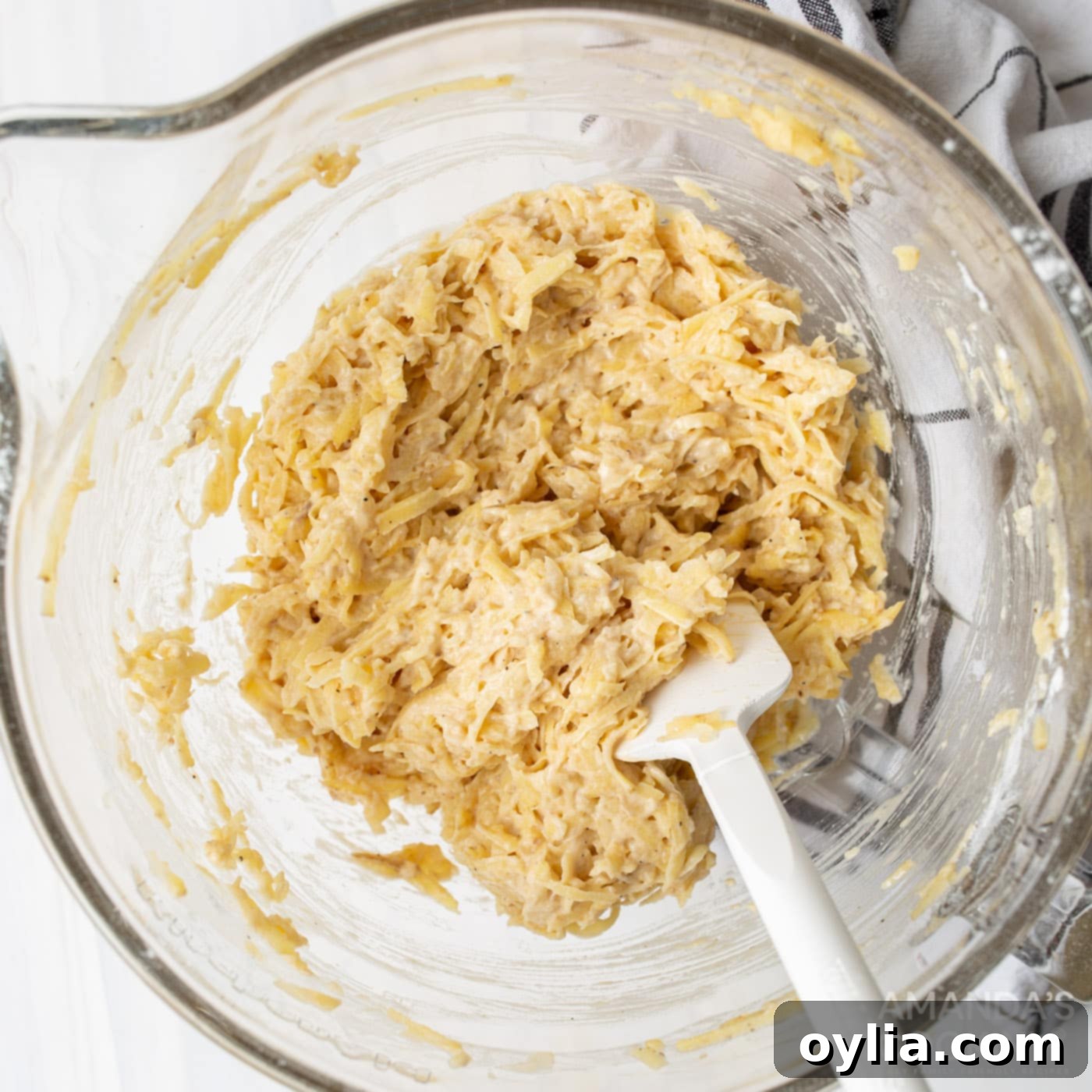 Bowl showing grated potato, onion, flour, egg, salt, and pepper thoroughly mixed together.
