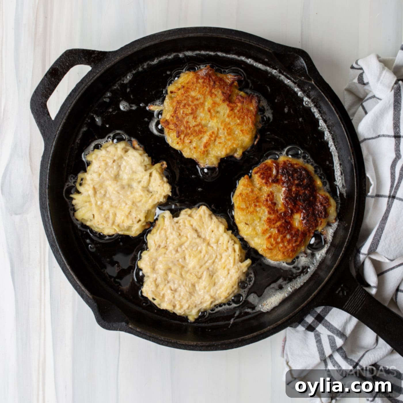 Several potato pancake patties frying in a hot skillet, turning golden brown.