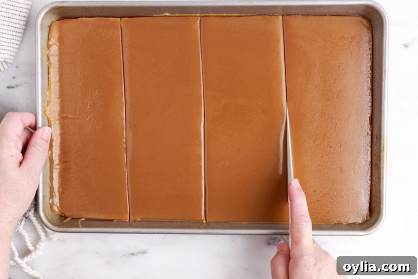 A knife slicing firm microwave caramels on a parchment-lined sheet pan.