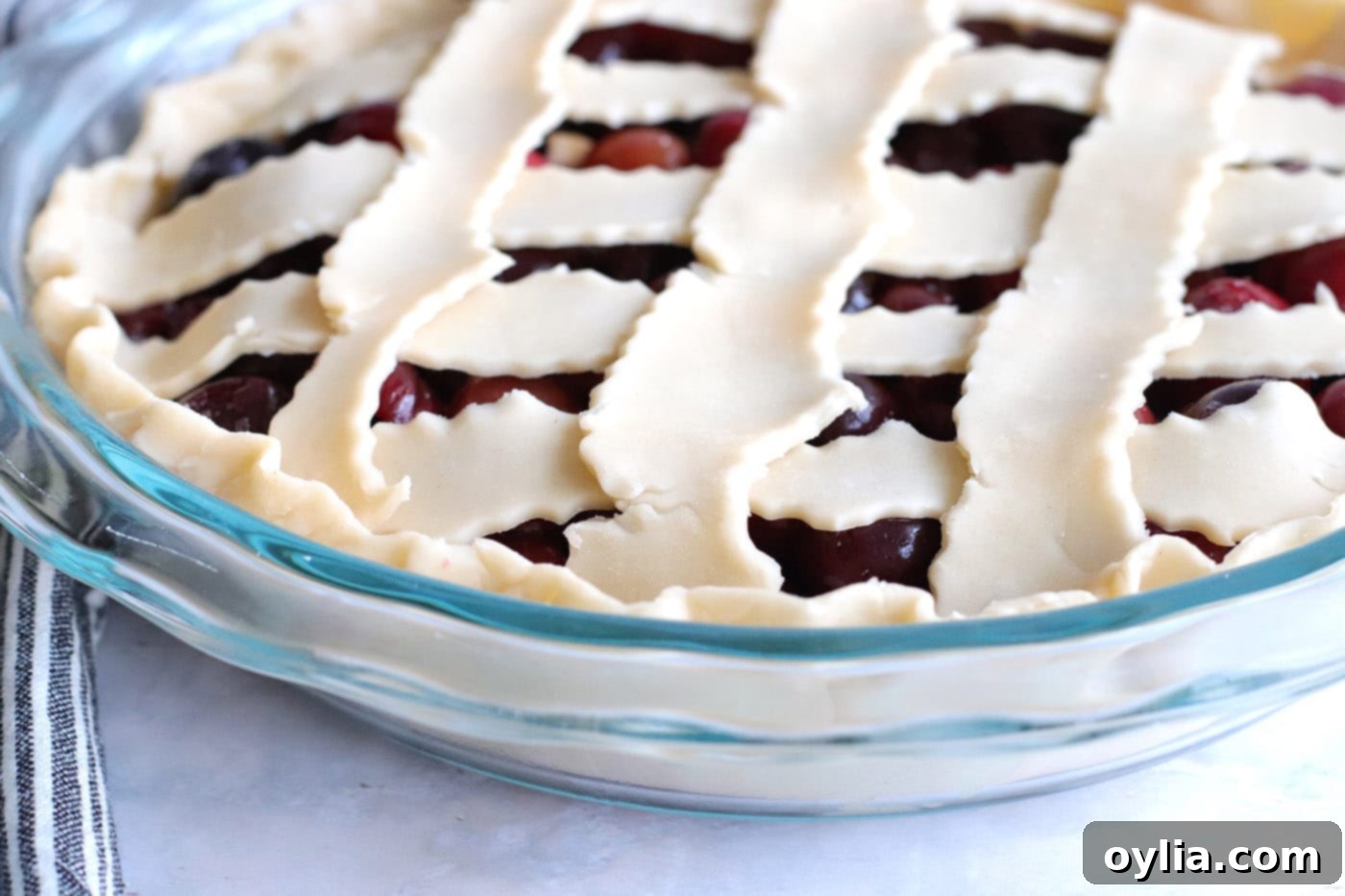 The edges of the cherry pie crust neatly tucked and crimped, preparing the pie for baking.