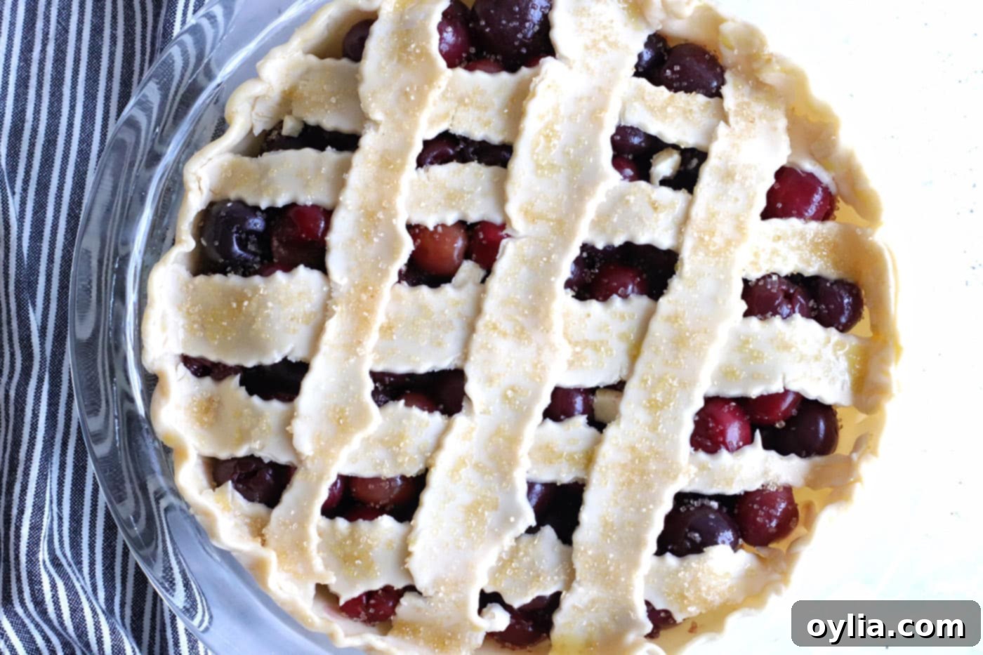 Unbaked cherry pie with egg wash and turbinado sugar sprinkled on its lattice crust, ready for the oven.