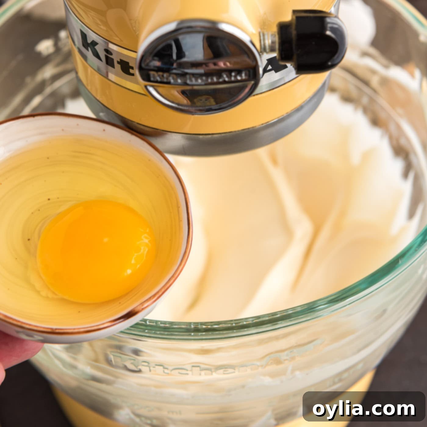 adding egg to stand mixer bowl with cheesecake filling