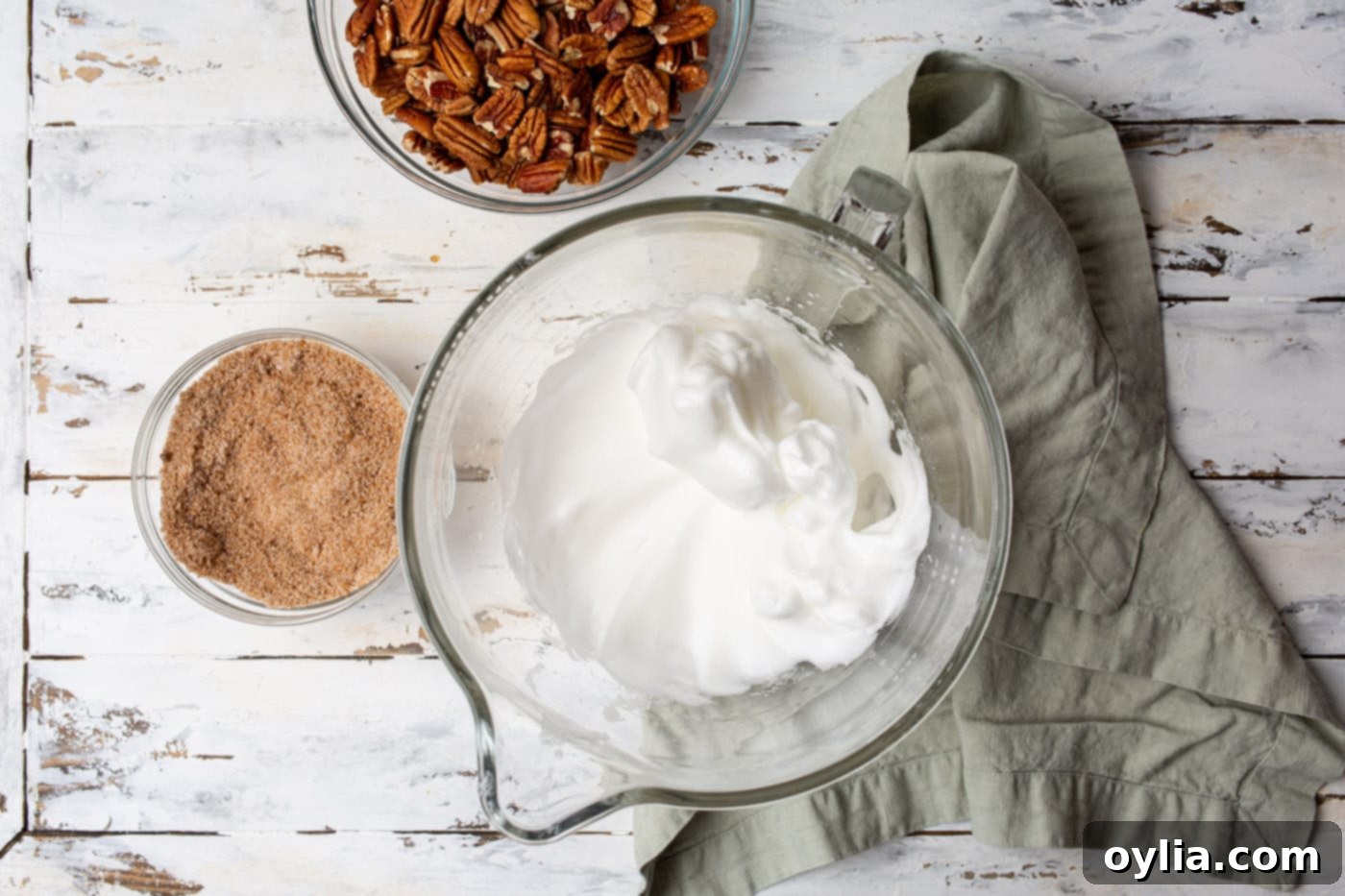 Egg whites, water, and vanilla extract whipped to stiff peaks in a stand mixer bowl.