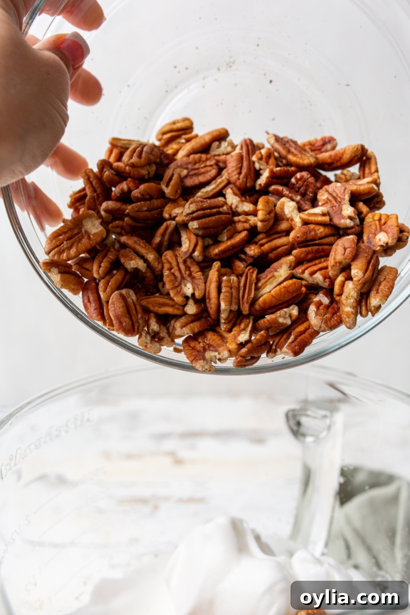 Pouring a bowl of pecan halves into whipped egg whites.