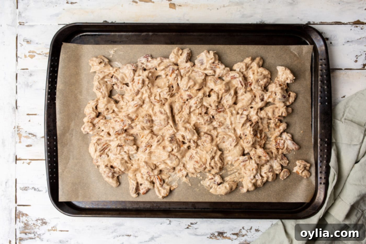 Candied pecans spread in a single, even layer on a parchment paper-lined baking sheet.