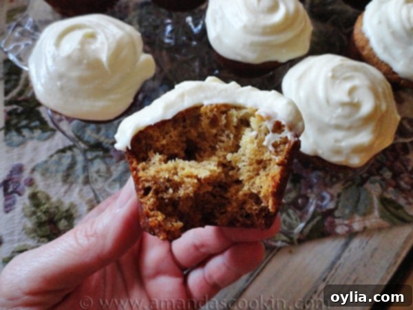 A close-up photo of a half-eaten banana cupcake, revealing its moist interior and creamy vanilla frosting, with more whole cupcakes blurred in the background.