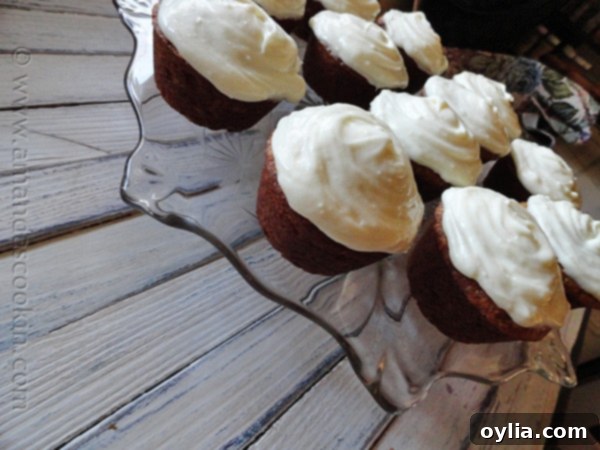 A collection of beautifully frosted banana cupcakes with vanilla cream cheese frosting, presented on a clear glass cake stand against a warm, inviting background.