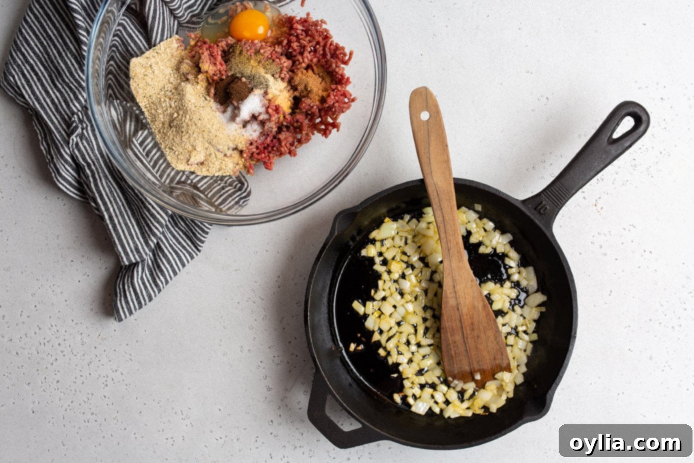 meatball ingredients in a mixing bowl with sauteed onions in a skillet