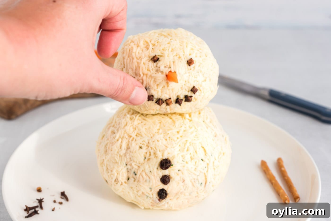 hand pressing cloves into snowman cheeseball
