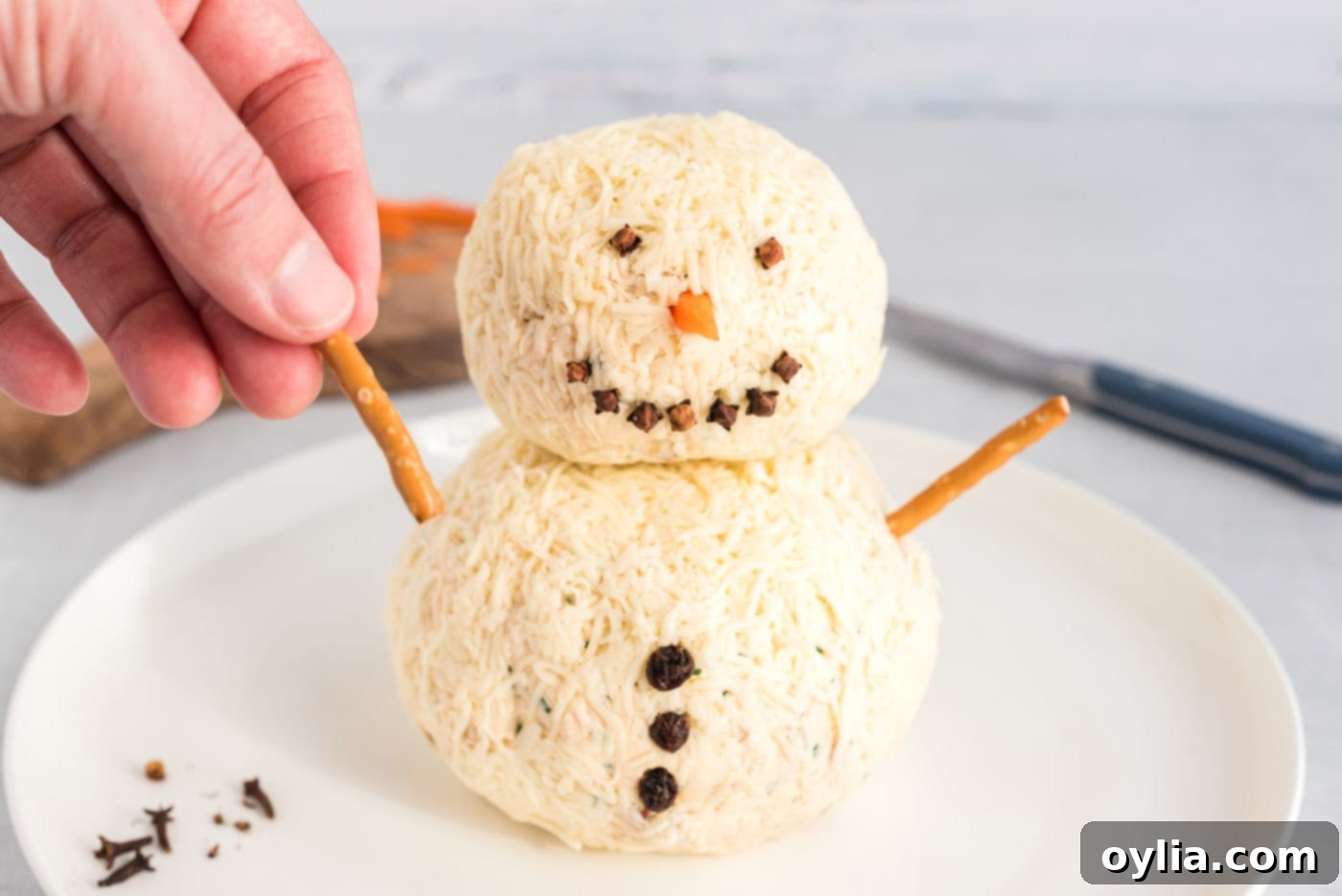 hand adding a pretzel stick to snowman cheeseball