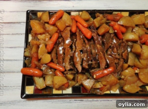 An overhead photo of a plate of slow cooker java brisket, sliced and served with a rich gravy and roasted vegetables.