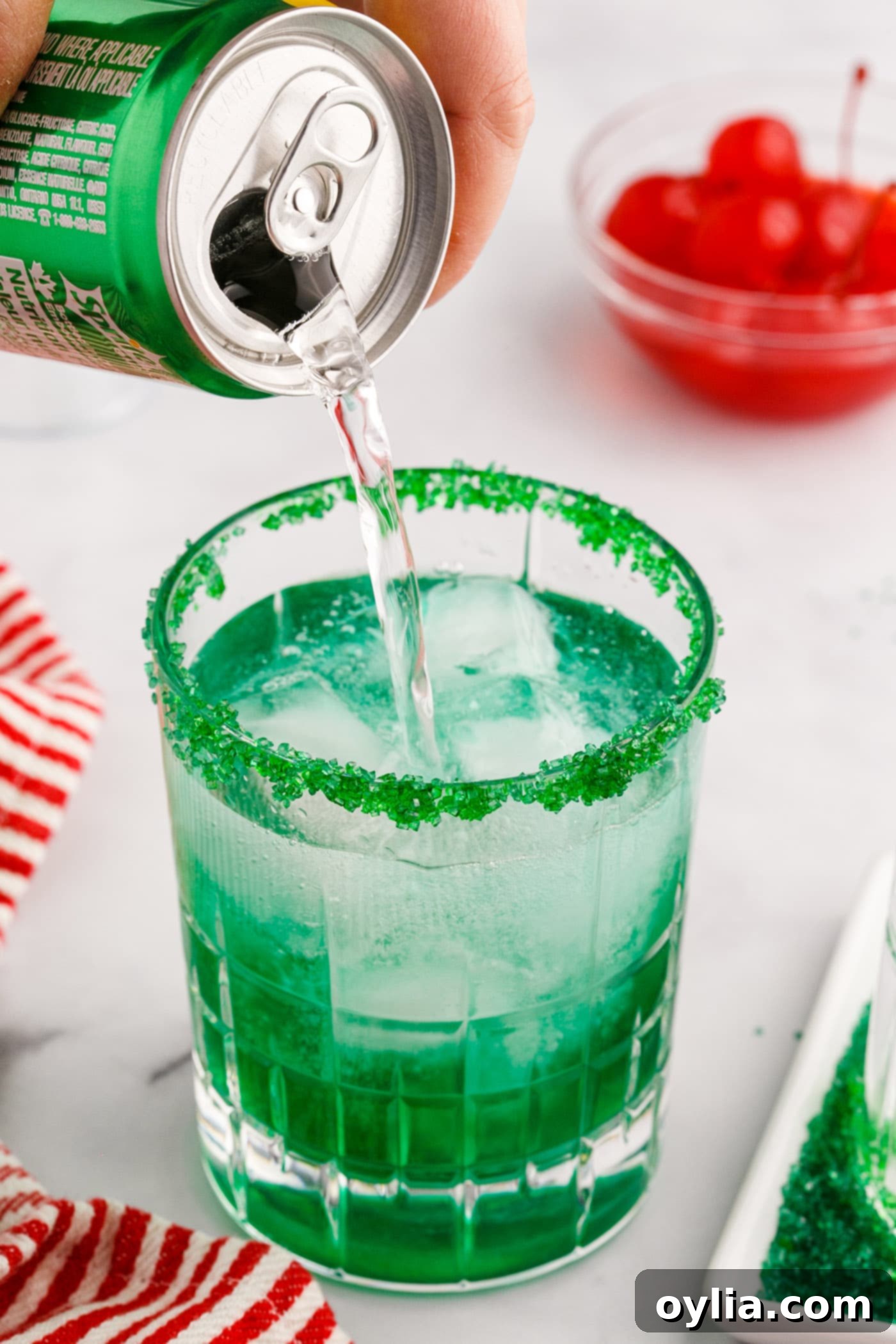 pouring lemon lime soda into grinch cocktail with sugared rim