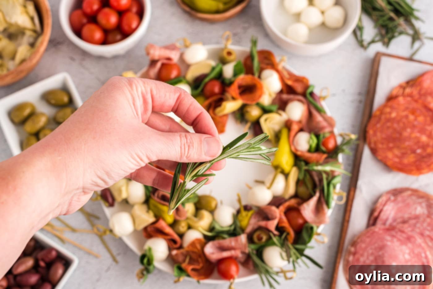 A hand adding fresh rosemary sprigs to the antipasto wreath for decoration.