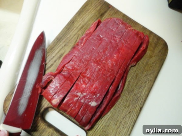 An overhead photo of thinly sliced flank steak arranged neatly on a wooden cutting board, prepped and ready for cooking.