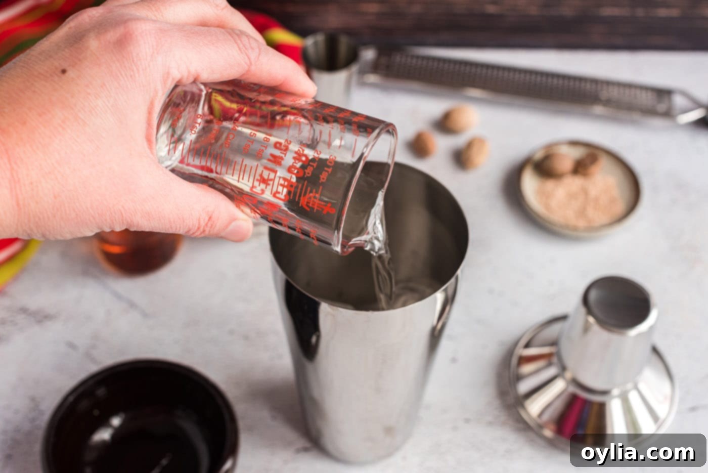 Pouring creme de cacao into a cocktail shaker filled with ice, a key step for a rich Brandy Alexander.