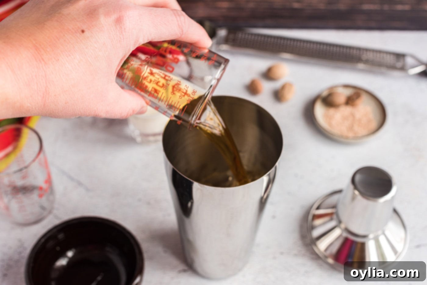 Adding cognac to a cocktail shaker, ensuring precise measurements for a balanced Brandy Alexander.