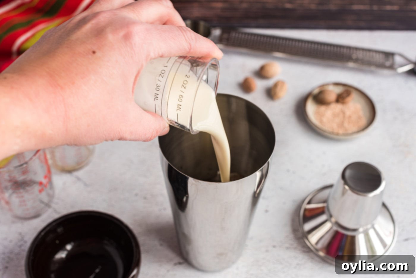 Pouring heavy cream into a cocktail shaker, essential for the creamy texture of the Brandy Alexander.