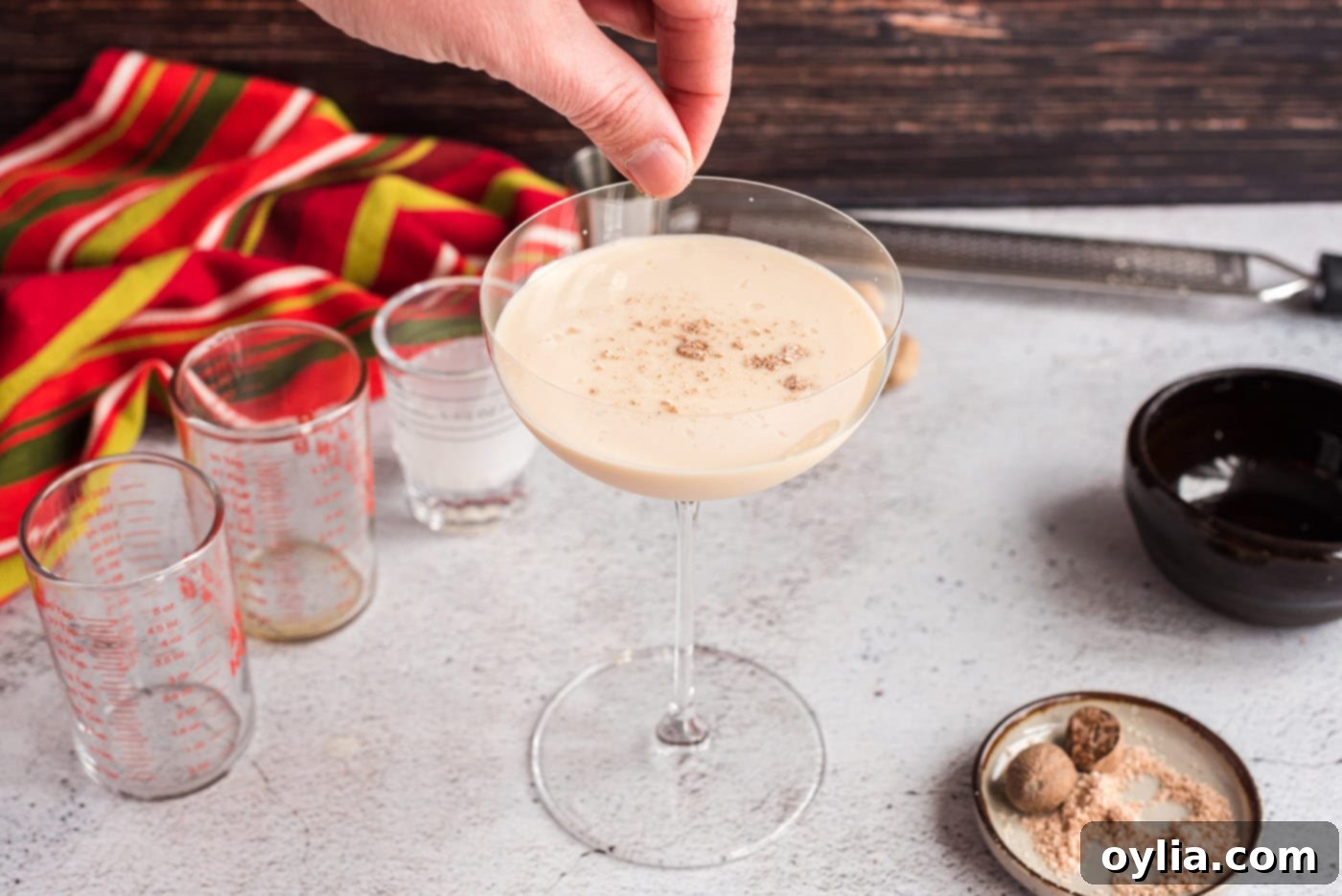 A hand sprinkling freshly ground nutmeg over a Brandy Alexander cocktail for an aromatic garnish.