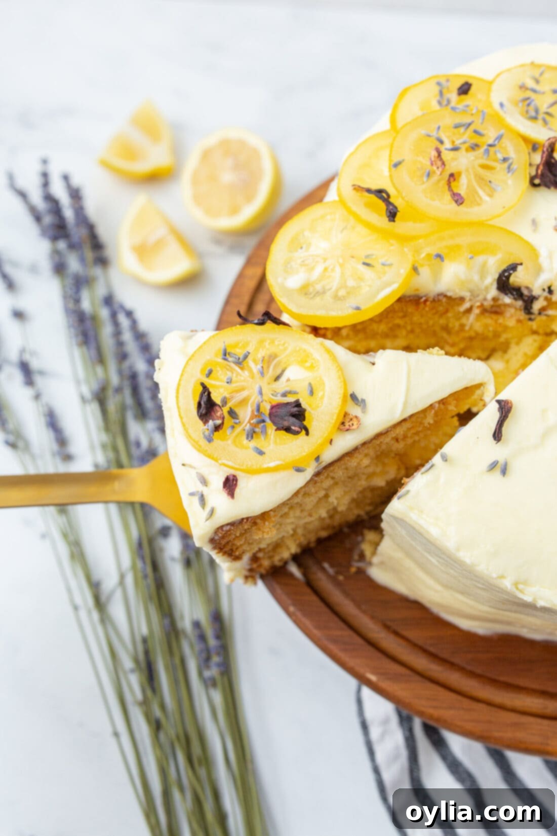A slice of beautiful tiered lemon cake being removed from a cake plate, showcasing the fluffy lemon buttercream and moist cake layers.