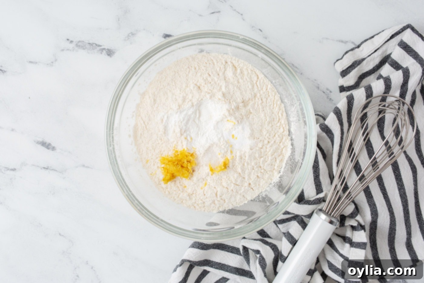 Dry ingredients for lemon cake, including flour, baking powder, baking soda, and salt, mixed in a bowl.