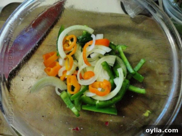 Sliced bell pepper, sweet peppers and onions in a clear bowl.