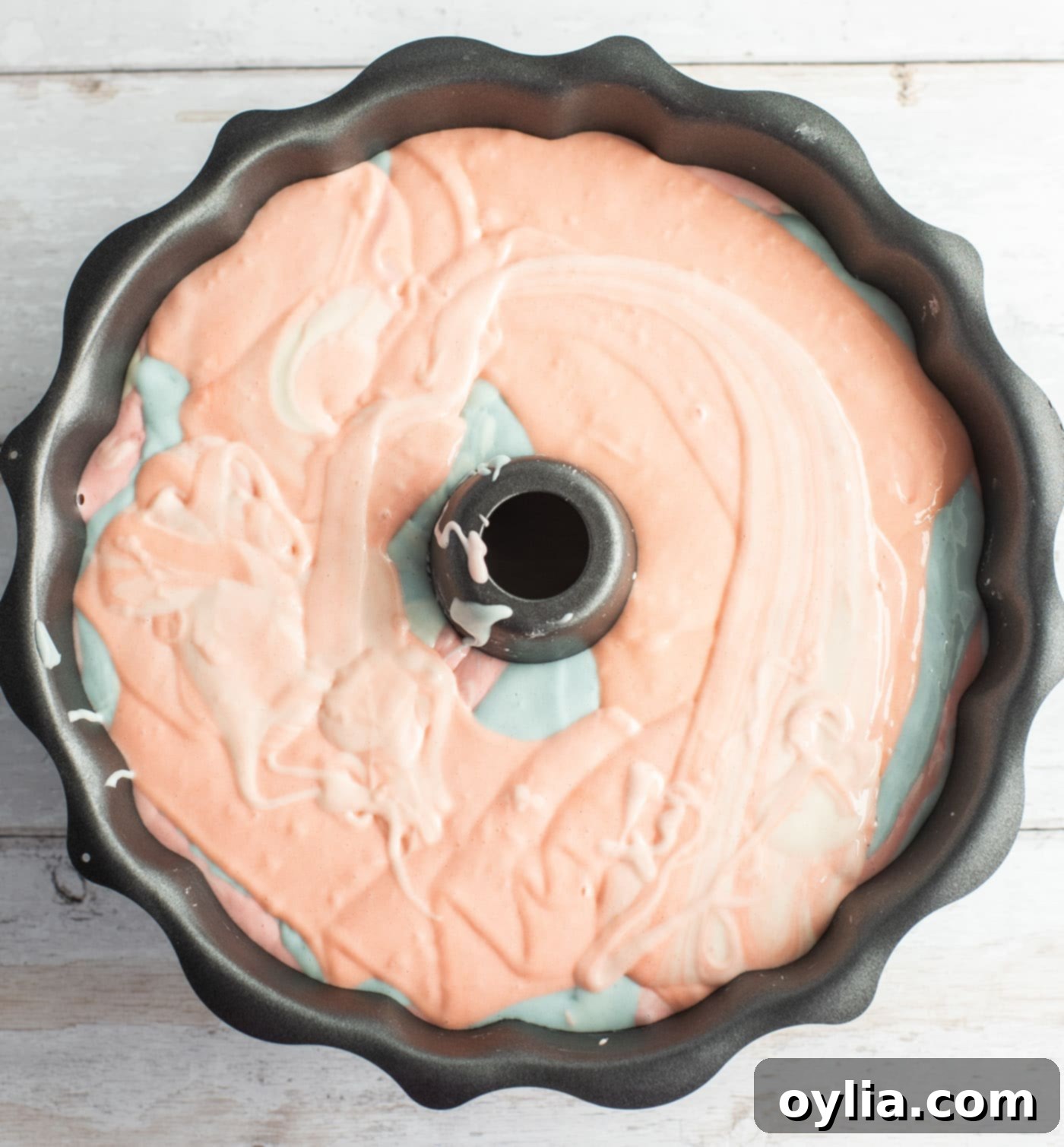 Multiple pastel colored cake batters layered in a bundt pan, ready for baking.