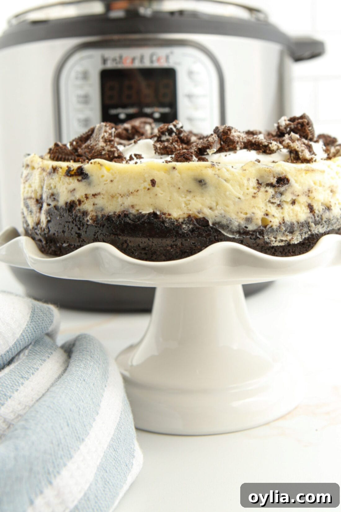 Instant Pot Oreo Cheesecake displayed on a cake plate with an Instant Pot in the background