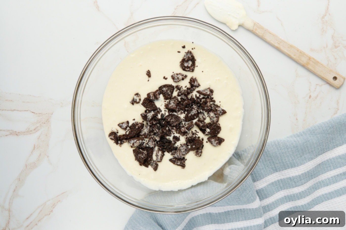 Roughly chopped Oreos being gently folded into the smooth cheesecake batter