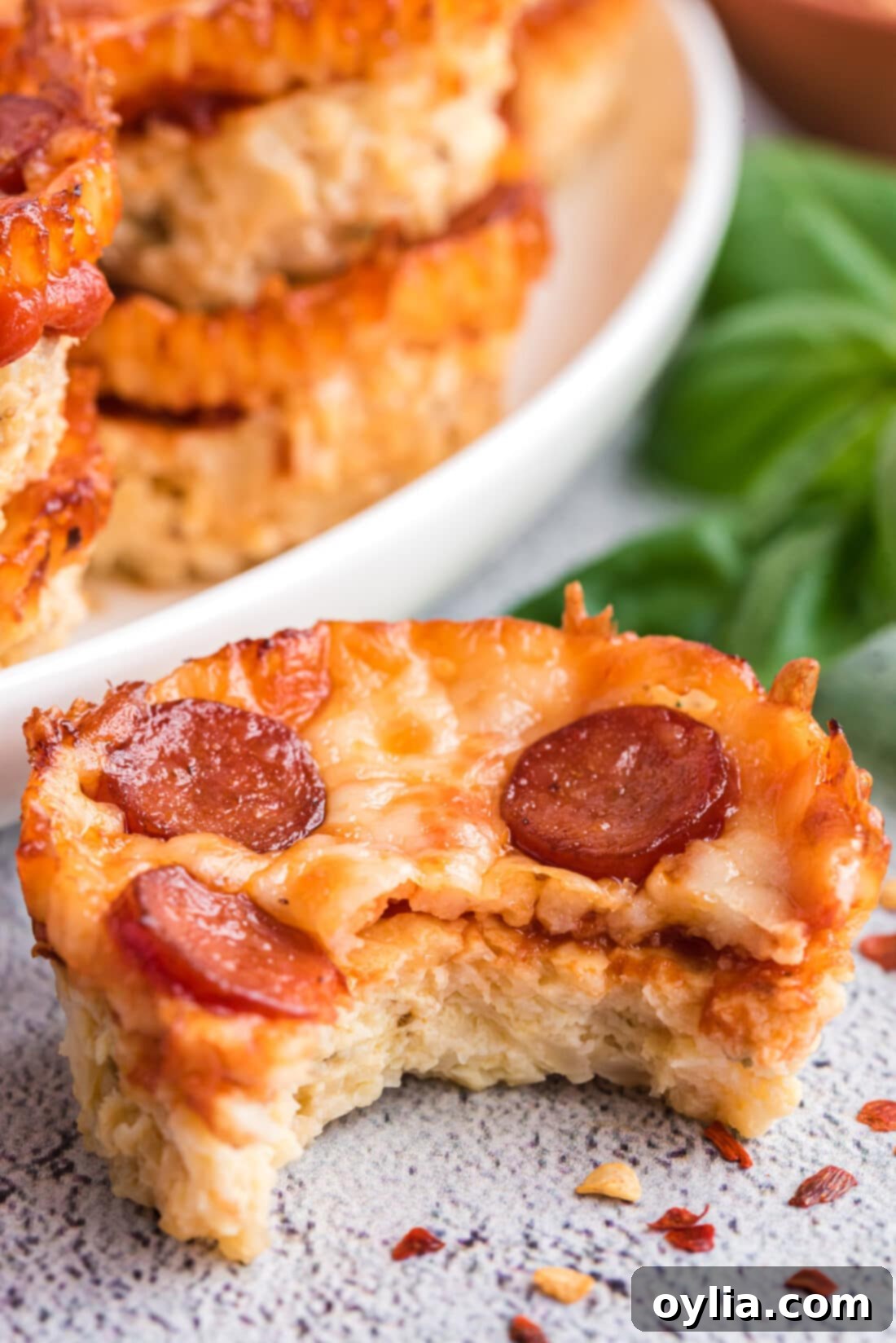 A close-up shot of a single baked cauliflower pizza bite with melted cheese and mini pepperoni, showing its appealing texture.