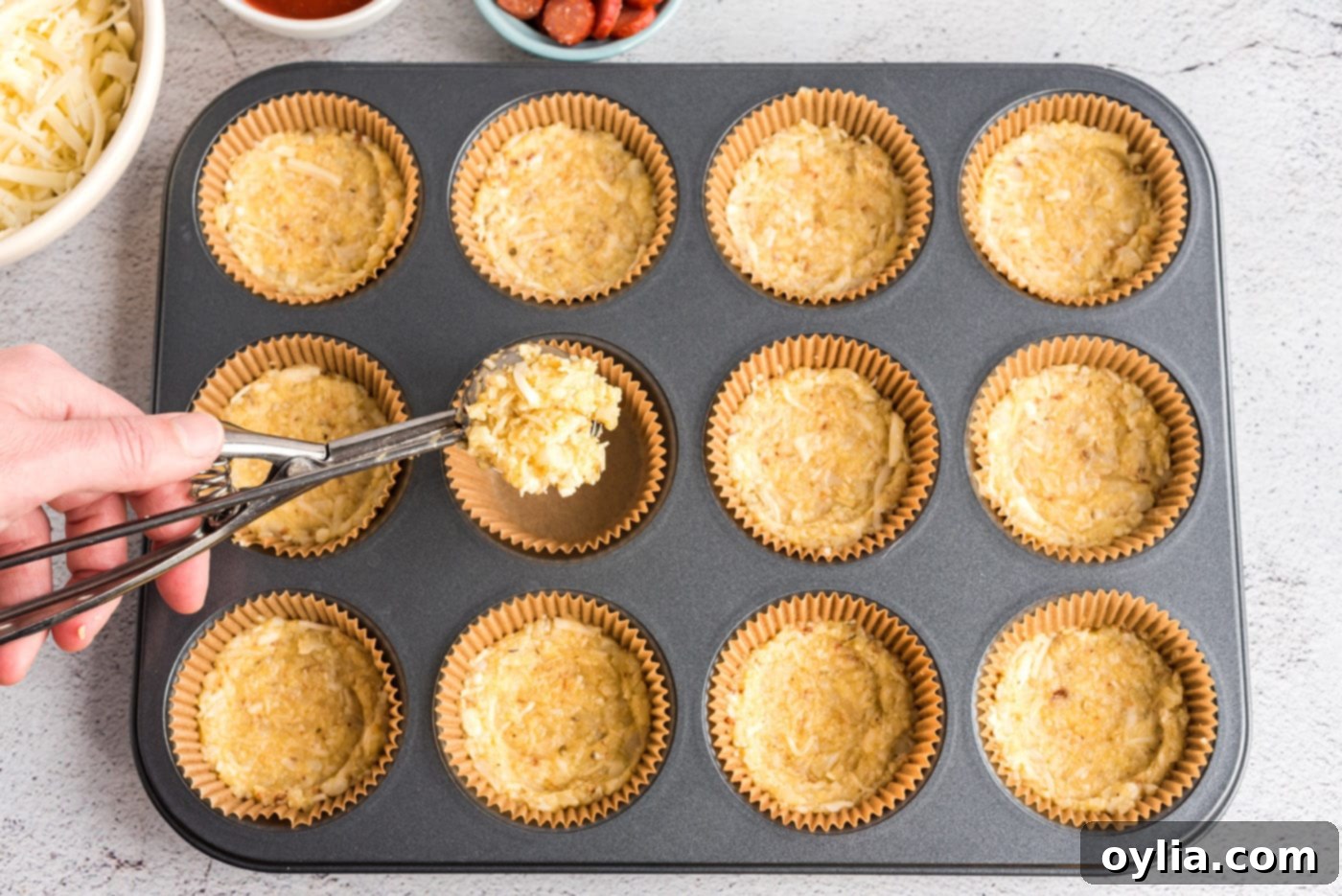 Cauliflower pizza crust mixture being pressed into a muffin tin to form mini crusts.