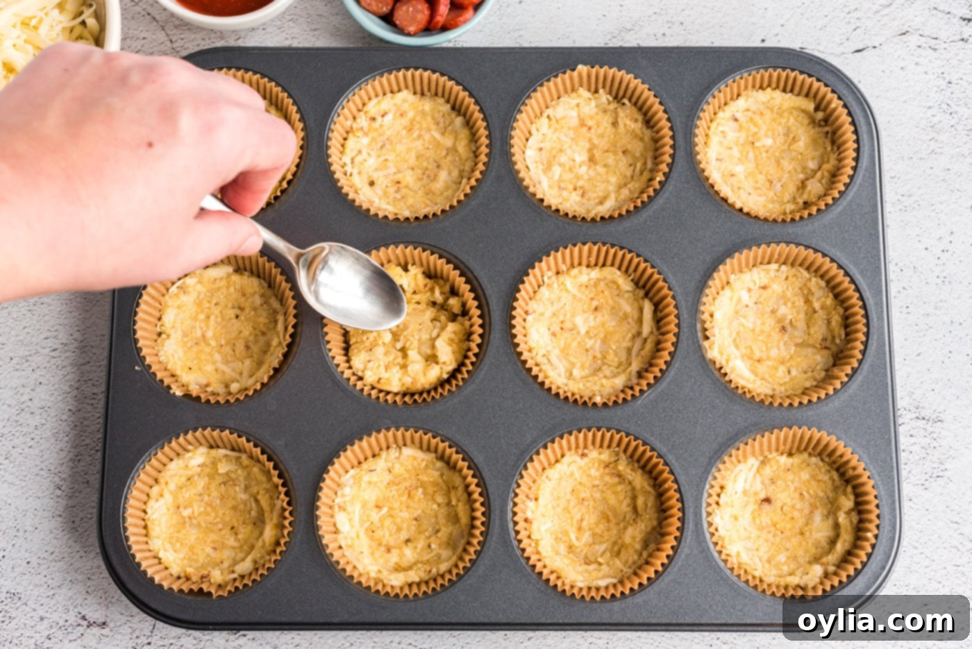 Flattening and shaping cauliflower crust mixture in a muffin tin to create uniform mini pizza bases.