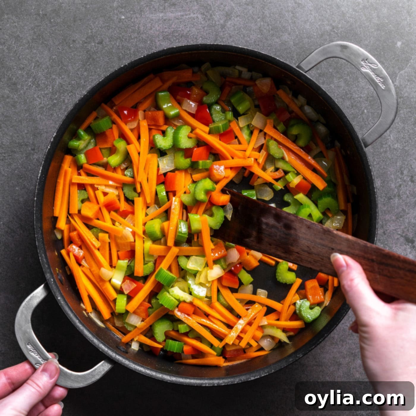 Sauteeing a colorful mix of celery, carrots, red bell pepper, and onion in a large skillet with melted butter.