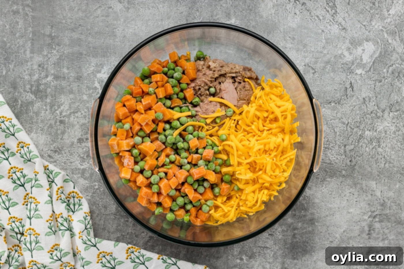 frozen peas and carrots with shredded cheese and tuna in a bowl, ready to be mixed